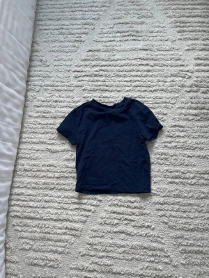 Mörkblå t-shirt från Divided - En enkel och stilren mörkblå t-shirt från Divided. T-shirten har korta ärmar och rund halsringning. Tillverkad i mjuk bomull som känns skön mot huden. Perfekt basplagg att matcha med allt.