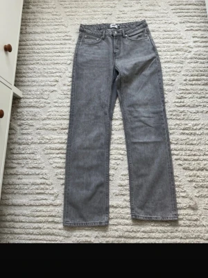 Grå raka jeans med fem fickor - Säljer ett par grå jeans med rak passform och klassisk femficksdesign. Jeansen har normal midja. Materialet är denim i bomull och färgen är en snygg ljusgrå ton som passar till det mesta.