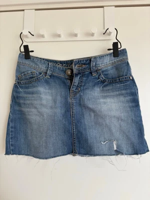 Blå jeanskjol från Esprit - Säljer en blå jeanskjol från Esprit Casual Denim. Kjolen är kort, har fem fickor, slitna detaljer och rå kant nedtill för en avslappnad look. Perfekt för dig som gillar en enkel men trendig stil.