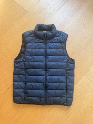 Uniqlo väst ultra light down puffer - Snygg svart dunväst med hög krage och horisontella sömmar. Västen har en stilren design med dragkedja framtill och två sidofickor. Perfekt att slänga över en hoodie eller tröja för extra värme. Materialet är lätt och smidigt, vilket gör den enkel att bära. Pris går att diskutera 