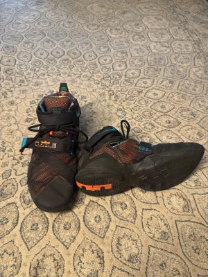  Nike LeBron Soldier 9 OKC - Säljer ett par Nike LeBron sneakers i svart med orange och blå detaljer. Skorna har en hög siluett, meshpaneler och kardborreband över vristen för extra support. Swoosh-logga i orange på sidan och coola färgdetaljer på sulan. Perfekta för dig som gillar basketstil. Basketskor LeBrons, ganska slitna, vill bara bli av med dom, storlek 48 EU  skickar samma dag efter dagen efter ;)