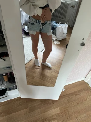 Ljusblå jeansshorts med rå kant - Säljer ett par ljusblå jeansshorts med rå, fransig kant och klassisk femficksdesign. De ä egenomsydda från jeans. Shortsen har hög midja och är tillverkade i bomull. Perfekta för varma dagar och ger en avslappnad vibe.