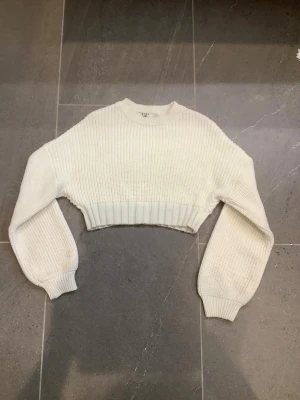 Vit cropped stickad tröja - Trendig vit cropped stickad tröja med bred ribbad mudd i midjan och vid ärmslut. Perfekt att styla med jeans eller kjol nu till hösten 🍂💗