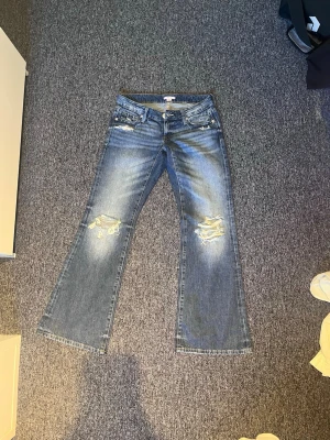 Blå bootcut jeans med slitningar - Säljer ett par blå bootcut jeans med slitna detaljer på knäna och ljus tvätt. Dom är från Gina och använts få gånger. Storlek S🩷