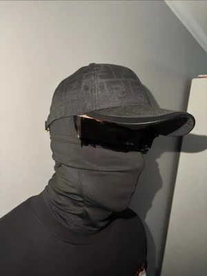 Svart Fendi keps  - Snygg svart Fendi keps med böjd skärm och diskret mönster i tyget. Kepsen har en klassisk form och är tillverkad i ett tygmaterial som ger en stilren look. Perfekt för dig som gillar en clean och modern stil. Helt ny bara använd för att ta bilder.