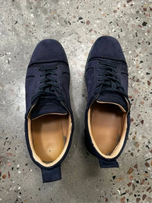 Loubs Mörkblå mockasneakers med röd sula - Snygga mörkblå sneakers i mocka med svarta skosnören och beige innersula. Skorna har en unik röd undersida och klassisk låg profil. Perfekta för dig som vill ha en stilren men ändå lite annorlunda sneaker.