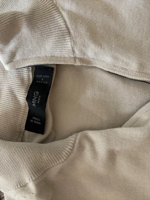 Beige halvzip-tröja från MNG MAN - Stilren beige tröja från MNG MAN med halvzip och ribbade muddar vid ärmslut och nederkant. Tillverkad i mjukt material som passar perfekt för lager-på-lager. 