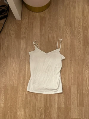Vit enkel linnetopp med smala band - Säljer en vit linnetopp med smala axelband och v-ringad hals. Toppen är ärmlös och har en enkel, clean design som passar till det mesta. Perfekt för varma dagar eller som lager under andra plagg.