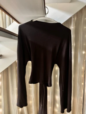 Brun knyt tröja från gina tricot - Säljer en brun långärmad topp med snygg knytning i ryggen och öppen detalj nedtill. Toppen har en tight passform och är croppad, vilket ger en trendig look. 