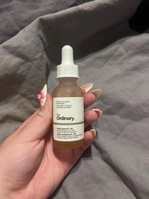 The Ordinary Lactic Acid 10% + HA serum - Säljer ett serum från The Ordinary med Lactic Acid 10% + HA. Kommer i en frostad glasflaska med vit pipett och etikett. Perfekt för dig som vill boosta hudvårdsrutinen med exfoliering och återfuktning.