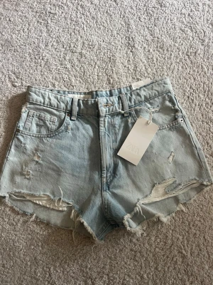 Jeansshorts från Zara - Säljer ett par ljusblå jeansshorts från Zara. Helt nya med prislapp kvar. 