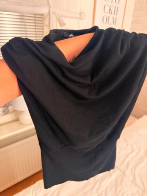 Svart axelbandslös tubtopp - Snygg svart axelbandslös tubtopp med bandeau-modell. Toppen har en enkel och clean design som passar perfekt till många olika outfits. Tillverkad i mjukt och stretchigt material för en bekväm passform.