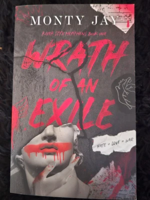 Wrath of an Exile av Monty Jay - En mörk och dramatisk pocketbok med titeln 'Wrath of an Exile' av Monty Jay. Omslaget har en staty i gråskala med röda grafiska detaljer och text, samt handritade illustrationer. Perfekt för dig som gillar spännande och intensiva berättelser.