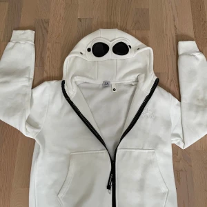 Vit hoodie från C.P. Company - Säljer en vit hoodie från C.P. Company med ikoniska goggles på luvan. Helt nytt skick, har andvänt 1 gång. Nypris: 3399kr, mitt pris kan självklart alltid diskuteras!🙌💯⚜️