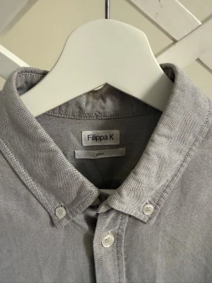 Grå skjorta från Filippa K - Stilren grå skjorta från Filippa K. Klassisk button-down krage, bröstficka och knappar framtill. Perfekt för dig som gillar en enkel men snygg look. Små fläckar men inget som märks under användning. Skriv vid fler frågor 🩶