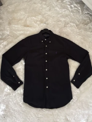 Ralph lauren skjorta - Svart Ralph lauren skjorta med lila logga  i riktig bra skick, använd vid endast ≈5 tillfällen. Skriv vid funderingar .