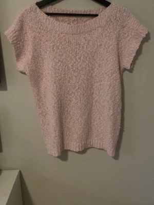 Ljusrosa stickad t-shirt - Mysig ljusrosa stickad t-shirt med korta ärmar och rund hals. Tröjan har en fluffig, mjuk struktur och är perfekt för dig som gillar en avslappnad och söt stil. Passar bra till jeans eller kjol för en chill look.