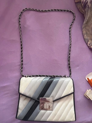 Randig handväska från Michael Kors - Säljer en äkta, stilren axelremsväska från Michael Kors i quiltat läder med silverfärgade detaljer. Modellen har ett vackert mönster i gråa, svarta och vita nyanser. Köptes för ca 5000 kr nypris men kan tänka mig att sälja den för 1000 vid snabb affär. Skicket är ganska bra med några repor på metallen och små fläckar som kan tas bort.