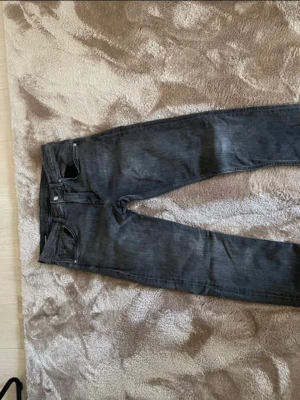 Grå jeans från J.Lindeberg - Snygga grå jeans från J.Lindeberg med klassisk femficksmodell och raka ben. Jeansen har en diskret logga på myntfickan och är tillverkade i ett mjukt denimtyg. Perfekta för dig som gillar en stilren och enkel look. 32/34
