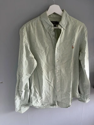 Grönvit randig skjorta - Snygg grön Ralph Lauren skjorta med vita ränder och klassisk button-down krage. Skjortan har långa ärmar, knappar framtill och en liten broderad logga på bröstet. 