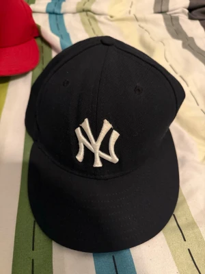 Svart New Era NY Yankees keps - Snygg svart keps från New Era med klassisk New York Yankees-logga broderad i vitt framtill. Kepsen har rak skärm och MLB-logga baktill. Tillverkad i bomull och polyester, perfekt för dig som gillar streetwear och sportig stil. One size
