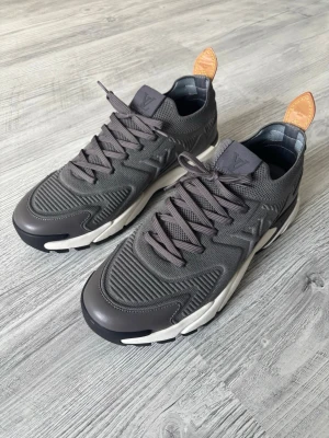 Grå sneakers - Snygga grå sneakers med stickad ovandel, detaljer i mocka och gummi samt vita och svarta sulor. Skorna har bruna läderflikar bak. Perfekta för dig som vill ha en exklusiv och modern look.