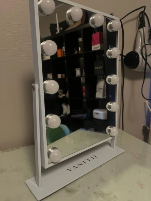 Vit sminkspegel med LED-lampor - Stilren sminkspegel från VANITH i vit metall med rektangulär form. Spegeln har 12 starka LED-lampor runt kanterna som ger perfekt belysning för makeup. Stabil fot och modern design gör den till ett snyggt tillskott på sminkbordet.