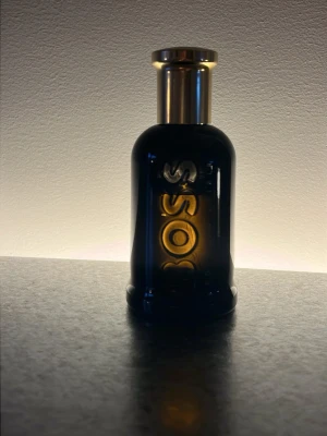 BOSS Bottled Elixir parfym - Säljer en BOSS Bottled Elixir parfym i en elegant mörk glasflaska med guldigt lock. Flaskan har en stilren design med BOSS-loggan i relief på framsidan. Perfekt för dig som gillar exklusiva och maskulina dofter. 50 ml. Se bild för mängd kvar.