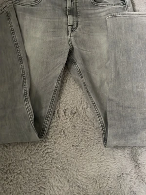 Grå tvättade raka jeans - Snygga grå jeans med tvättad look och raka ben. Klassisk femficksmodell med svarta sömmar på bakfickorna. Perfekta för en avslappnad och trendig stil. Materialet är denim och färgen är ljusgrå.