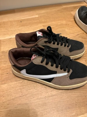 Nike Air svart/brun sneaker - Snygga Nike Air sneakers i svart och brunt med vit swoosh på sidan. Skorna har lågt skaft, svart snörning och brun insida. Ovandelen är i mocka och textil, vilket ger en skön och trendig look. Perfekta för dig som gillar streetwear och vill ha något unikt.