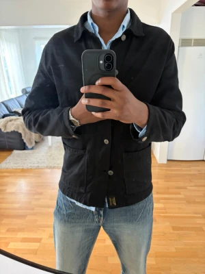 Svart overshirt i bomull - Stilren svart overshirt med knappar framtill och två stora fickor. Jackan har en klassisk krage och är tillverkad i bomull, vilket gör den både bekväm och lätt att bära. Perfekt att slänga över en skjorta för en clean look eller direkt över en T-shirt. Riktigt stilig passform tidigare Zara kollektion. Defekt vid armen under knappen ingenting som syns när man bär den. 