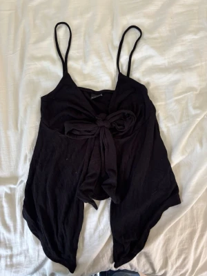 Svart linnetopp med knyt från Gina Tricot - Säljer en svart linnetopp från Gina Tricot med smala axelband och snygg knytning framtill. Toppen har en asymmetrisk nederkant och är perfekt för dig som vill ha en trendig och luftig look. Materialet känns mjukt och lätt.