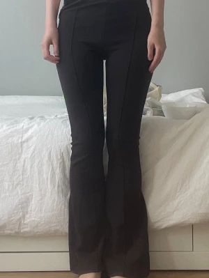 Bruna utsvängda mjukisbyxor - Säljer ett par bruna mjukisbyxor med utsvängda ben och hög midja. Byxorna har söm längs framsidan som ger en snygg detalj och sitter tight över låren. Perfekta för en chill och trendig look. Obs: trasig dragkedja.