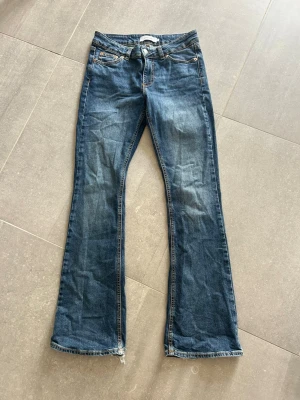 Blå bootcut jeans från junkyard - Säljer ett par klassiska blå bootcut jeans. Jeansen har fem fickor, normal midja och kontrastsömmar. Perfekta för dig som gillar en avslappnad och trendig look. Materialet är denim i bomull. Slitningar vid hälarna då jag gått på dom annars bra skick.