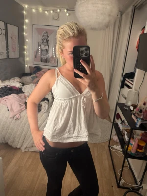 Vit ärmlös linnetopp med spets - Söt vit linnetopp med tunna axelband och v-ringad hals. Toppen har en luftig passform och fina spetsdetaljer längs kanterna. Perfekt för varma dagar och enkel att styla med jeans eller kjol.