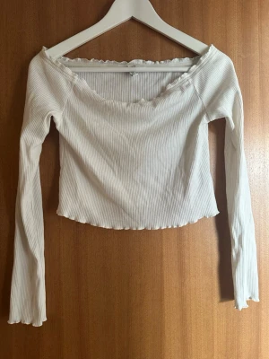 Vit ribbad långärmad topp H&M - Säljer en vit ribbad långärmad off shoulder topp från H&M Basic. Toppen har en croppad passform, lätt vågig kant vid halsringning och nederkant samt en bred, något offshoulder urringning. Perfekt att styla med jeans eller kjol.