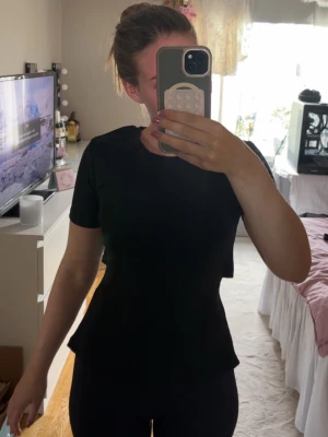 Svart t-shirt med öppen rygg och knyt - Säljer en svart t-shirt med korta ärmar och öppen rygg med knytband. T-shirten har en figurnära passform och är tillverkad i ett mjukt bomullsliknande material. Perfekt för dig som vill ha en enkel men ändå trendig look.