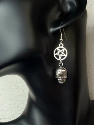 Unika Handgjorda Pentagram & Skull-örhängen – One of a Kind Goth Punk Alternative - Handgjorda nya örhängen med pentagram och dödskalle för dig som gillar goth, alternative, punk och rock. Det här är det enda paret jag har gjort – ett äkta one of a kind-smycke. 5,5 x 1,2 cm. Unisex. Allergivänliga krokar och nya gummistoppar medföljer. Lätta och bekväma att bära. Ett unikt statement som ingen annan kommer att ha. Jag ger gärna bundlerabatt vid köp av flera varor.