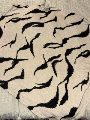 Beige poncho med svart mönster - Accessoar från Street One i beige med svart abstrakt mönster. Tunt och mjukt tyg som ger en avslappnad känsla och kan användas på flera olika sätt för att lyfta din outfit. Materialet känns lätt och smidigt, och designen är riktigt unik.