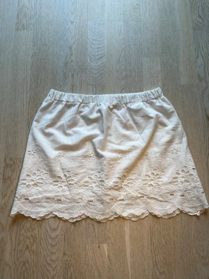 Vit kortkjol med broderade blommor - Söt vit kortkjol med elastisk midja och broderade blommor samt spetsdetaljer längs nederkanten. Kjolen har en romantisk känsla och passar perfekt till sommaren. Tillverkad i bomull för en luftig och bekväm känsla. Tveka inte på att skriva en fråga eller be om fler bilder.🌸🌸