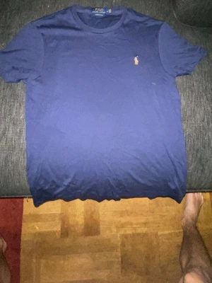 Blå t-shirt från Polo Ralph Lauren äkta  - Snygg marinblå t-shirt från Polo Ralph Lauren med klassisk rund hals och liten broderad logga på bröstet. Modellen är custom slim fit och passar perfekt till jeans eller shorts. Tillverkad i mjuk bomull för skön känsla hela dagen.