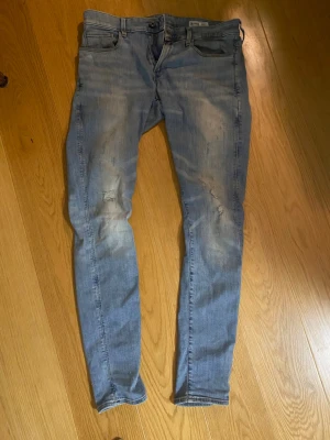 Ljusblå skinny jeans från G-Star RAW - Säljer ett par ljusblå skinny jeans från G-Star RAW med slitningar på knäna och klassiska fem fickor. Jeansen har en tvättad look och är tillverkade i denim med stretch för extra komfort. Storlek 33/34