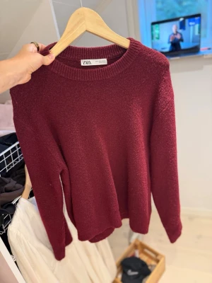 Vinröd stickad tröja från ZARA - Mysig vinröd stickad tröja från ZARA med rund halsringning och långa ärmar. Tröjan har en enkel, klassisk design med ribbstickade muddar vid hals, ärmslut och nederkant. Perfekt för lager på lager och höstiga dagar.