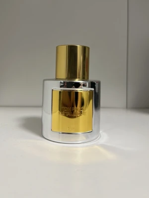Tom Ford Metallique parfym 50 ml - Säljer en Tom Ford Metallique parfym i en lyxig flaska med spegelblankt silver och gulddetaljer. Flaskan har en rund form och ett elegant guldlock med TF-logga på toppen. Rymmer 50 ml och är perfekt för dig som gillar exklusiva dofter.