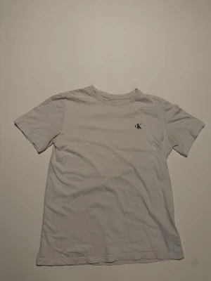 Vit t-shirt från Calvin Klein - Vit t-shirt från Calvin Klein med liten CK-logga broderad på bröstet. Klassisk rund halsringning och korta ärmar. Tillverkad i mjuk bomull för en skön känsla och enkel stil.