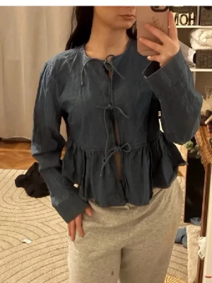 Blå volang jeanstopp med knytning - Supersöt blå blus i denim material med volang nedtill och tre knytningar framtill. Långärmad och med rund halsringning. Perfekt för en chill och trendig look. Perfekt till hösten🍁🍁Köptes för 1100kr