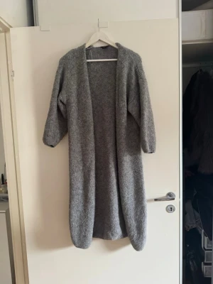 Lång grå stickad kofta från Lindex - Mysig lång grå stickad kofta från Lindex. Koftan har öppen front, långa ärmar och är gjord i ett mjukt, grovstickat material. Perfekt att slänga över en outfit för extra värme och stil❤️har inte använt den mer än 3 gånger 🩷