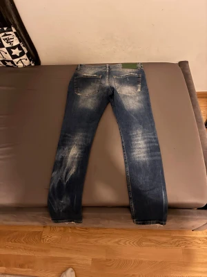 Blå Dsquared2 jeans med slitningar w29 l32 - Säljer ett par blå jeans från Dsquared2 med snygga slitningar och tvättade detaljer. Jeansen har raka ben, två bakfickor och en grön patch med Dsquared2-logga bak i midjan. Perfekta för dig som gillar en trendig och avslappnad stil.
