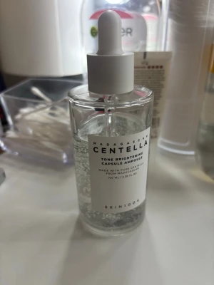 Centella Tone Brightening Ampoule - En genomskinlig toner i glasflaska med pipett från SKIN1004. Innehåller kapslar som syns i vätskan och är framtagen med centella från Madagaskar. Perfekt för dig som vill ha en fräsch och återfuktande bas i din hudvårdsrutin.