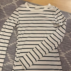 Randig ribbad långärmad topp - Säljer en vit ribbad topp med svarta horisontella ränder. Toppen har lång ärm och rund halsringning, perfekt för en enkel och stilren look. Materialet är mjukt och stretchigt för skön passform.